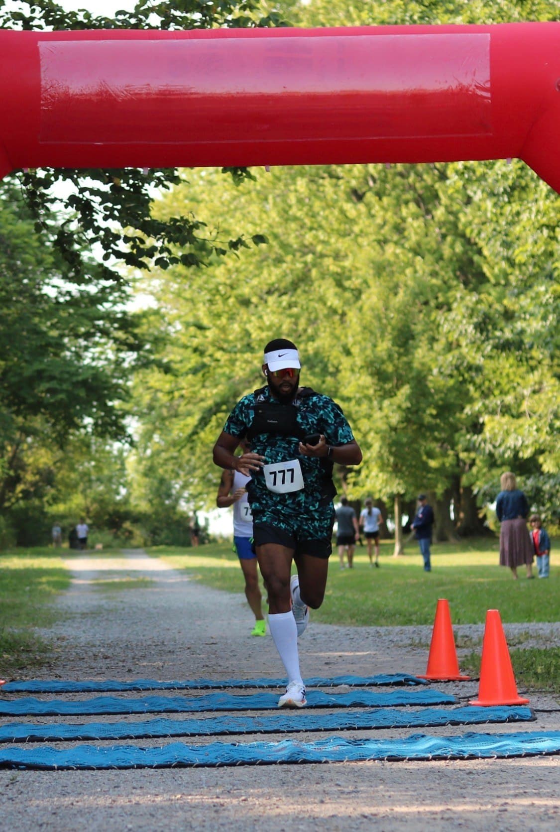 Tiye Martin running toward a red finish arch on a gravel path, wearing race bib 777.